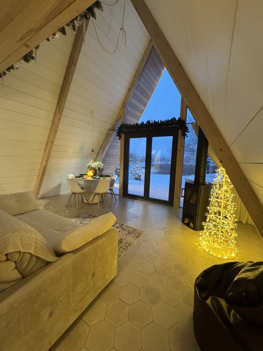 Гостиная A-frame дома зимой с диваном, дровяной печью, наряженной ёлкой и панорамным окном на снег