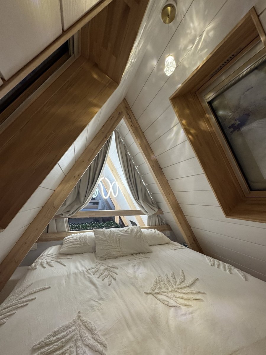 Спальня под коньком крыши A-frame с белым постельным бельём и двумя треугольными окнами